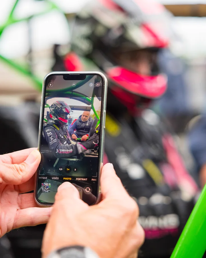 Un téléphone filme Dominique Palanque en échange avec un pilote casqué, installé dans sa voiture