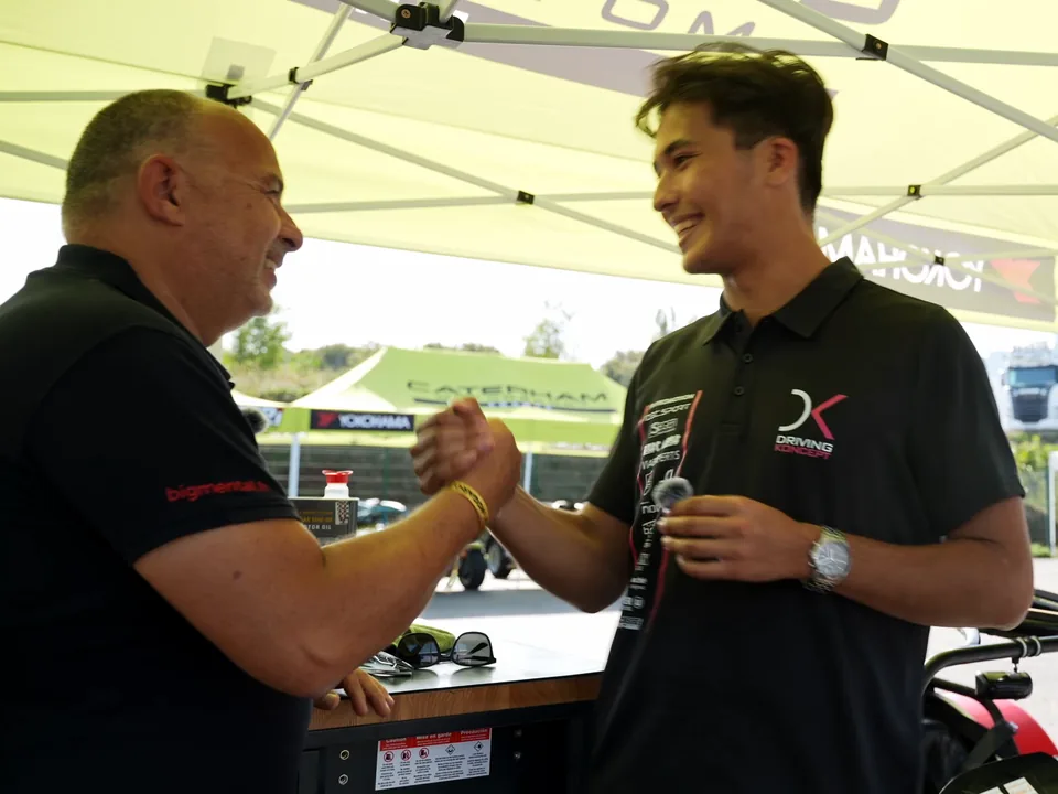 Dominique Palanque serre la main d'un jeune pilote sous la tente de son team, dans le paddock