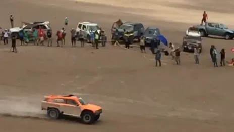Un buggy de rallye raid soulève la poussière dans le désert, devant les spectateurs