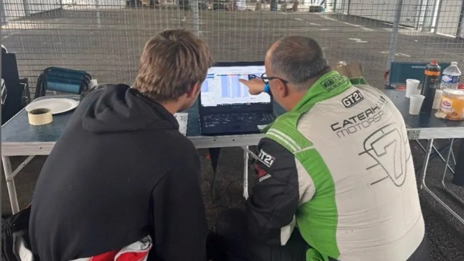 Dominique Palanque, en tenue Caterham Motorsport, analyse des données sur un ordinateur avec un jeune pilote
