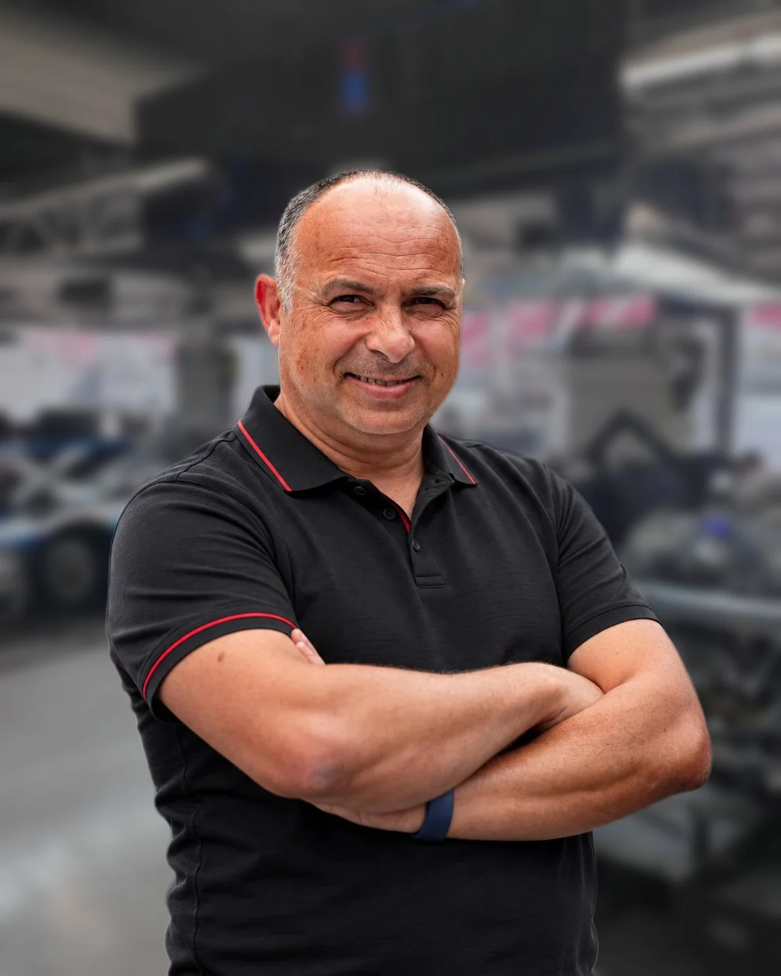Dominique Palanque, en polo noir, bras croisés et souriant dans le box d'un team d'endurance